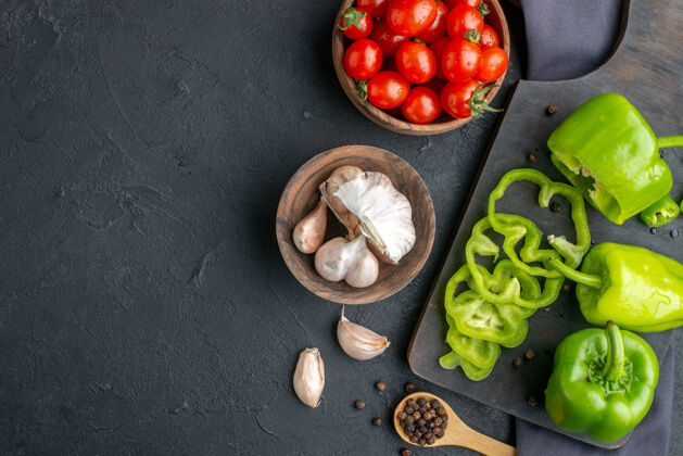 碗整个切好的切好的青椒在木制砧板上俯视 西红柿在碗里 大蒜素在深色毛巾上 在黑色表面的左侧青椒水果切