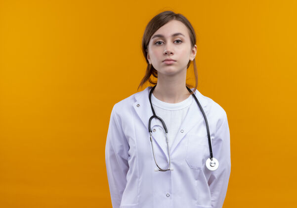 橙色严肃的年轻女医生穿着医用长袍和听诊器看着孤立的橙色空间与复印空间穿严重女