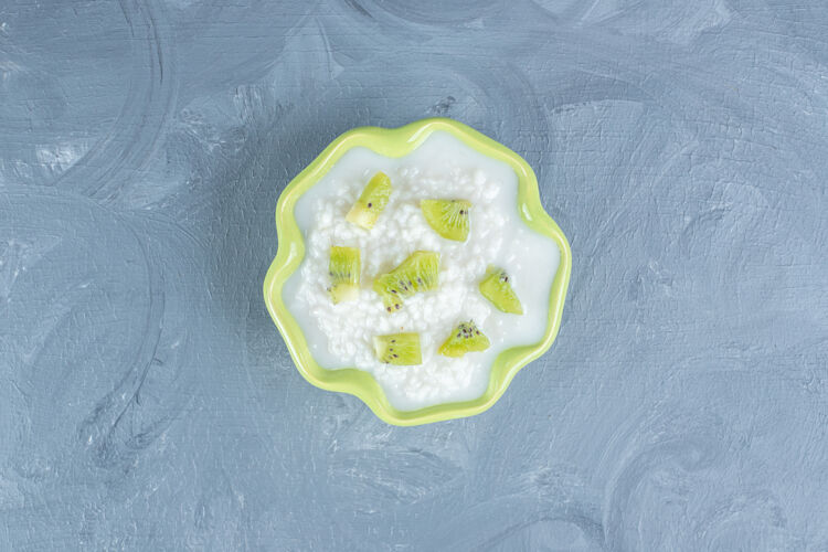 美味绿色的碗里装满了米饭布丁 上面放着奇异果碎片放在大理石桌上猕猴桃碗牛奶
