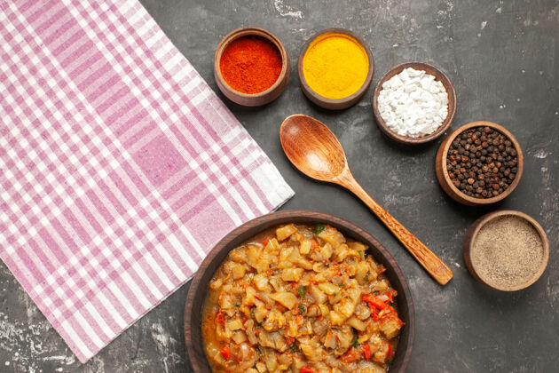 蔬菜顶视图烤茄子沙拉碗 木勺 不同的香料碗和厨房毛巾在黑暗的表面木头胡椒午餐