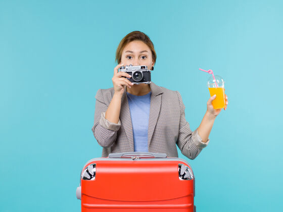 假期前景度假中的女性手持新鲜果汁和相机在淡蓝色的办公桌上海上度假旅行相机肖像光