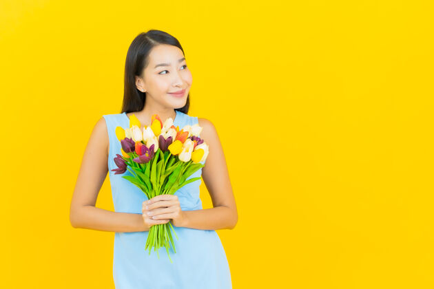 花束在黄色的墙上画着美丽的亚洲年轻女子带着鲜花微笑护理女孩美丽