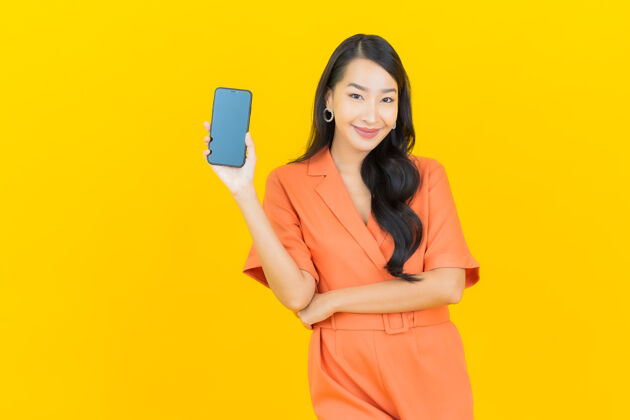 手持肖像美丽的亚洲年轻女子微笑着智能手机上的黄色购物设备手机