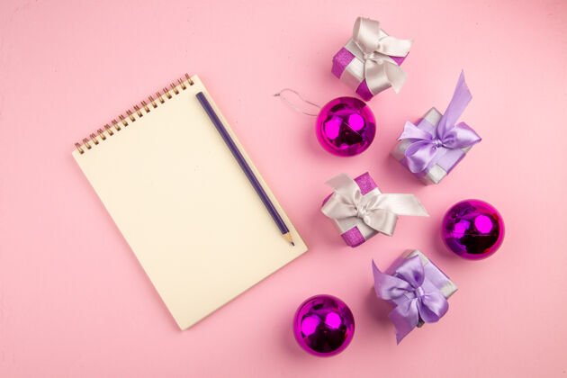 圣诞节顶视图的小礼物与记事本和玩具在粉红色的表面框架花家庭