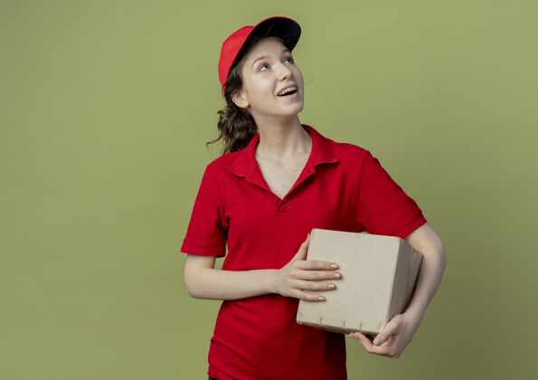 纸箱令人印象深刻的年轻漂亮的送货女孩在红色制服和帽子仰视和举行纸箱孤立在橄榄绿的背景与复制空间漂亮印象红色