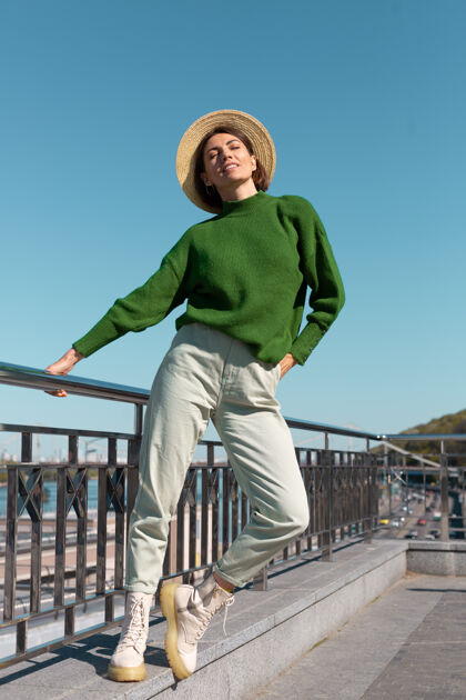 旅游穿着绿色休闲毛衣 戴着帽子的时尚女士在户外的桥上欣赏河景 享受夏日阳光明媚的日子城市人优雅