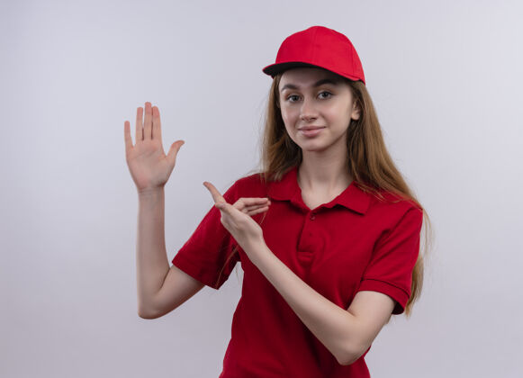 提高穿着红色制服的自信的年轻送货女孩举起手 指着孤立的空白处指向年轻手