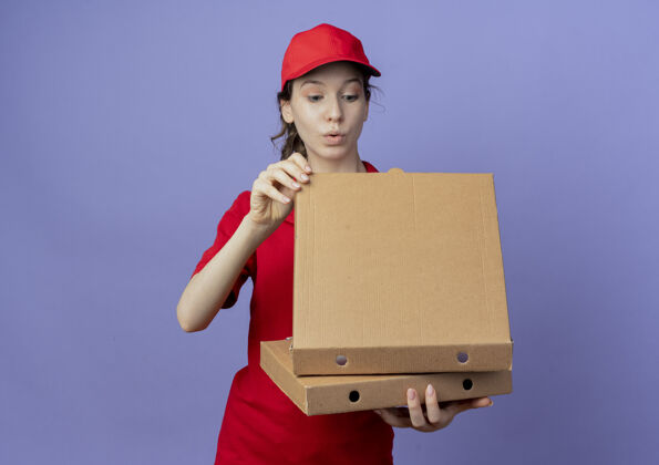 紫色令人印象深刻的年轻漂亮的送货女孩穿着红色制服和帽子举行比萨饼包 并期待在紫色背景与复制空间隔离包内女孩制服帽子
