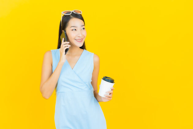 亚洲人肖像美丽的亚洲年轻女子微笑与智能手机在黄色墙上肖像电话手持