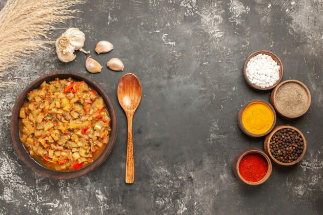 美味顶视图烤茄子沙拉在碗里油瓶大蒜木勺在碗里不同的香料在黑暗的表面玉米香料深色