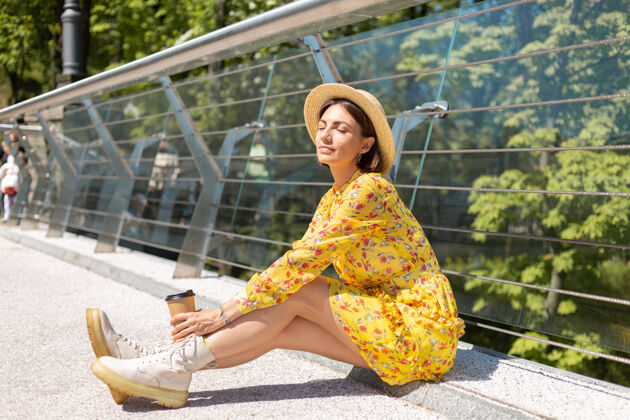 女人穿着黄色夏装 戴着帽子 喝着咖啡 享受阳光的女人的户外肖像享受女性人