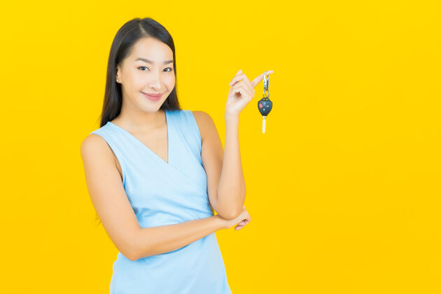 购买画像美丽的亚洲年轻女子微笑与车钥匙在黄色墙上展示亚洲人道路