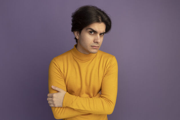 感觉可疑的年轻帅哥穿着黄色高领毛衣双手交叉隔离在紫色的墙上男人高领毛衣帅气