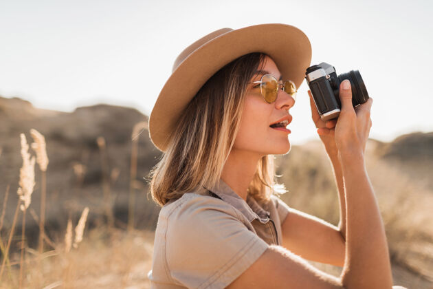 沙漠穿着卡其色长裙的美丽时尚的年轻女子在沙漠中旅行 在非洲旅行 戴着帽子在老式相机上拍照时尚非洲美丽