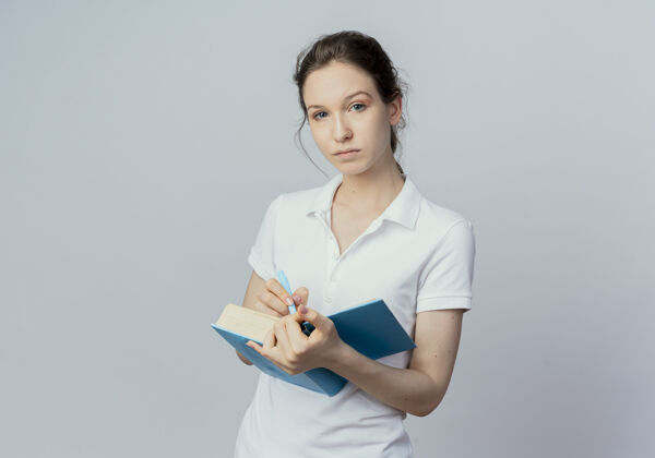 漂亮自信的年轻漂亮的女学生拿着打开的书和笔 看着相机隔离在白色背景与复印空间开放抱着笔