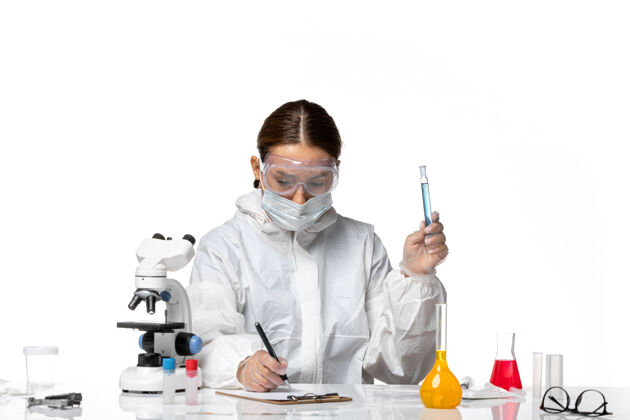 科学家前视图：女医生穿着防护服 戴着口罩 拿着装有白色背景病毒冠状病毒溶液的烧瓶保护专业面具