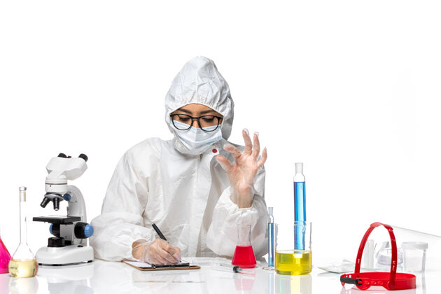 白人前视图穿着特殊防护服的女化学家正在检查样本 并在白色背景上书写病毒化学成分可预防大流行健康健康样品化学