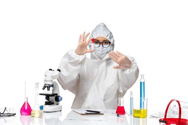 桌子正面图穿着特殊防护服的女化学家拿着白桌子上的空瓶子病毒健康化学病毒套装病毒视图