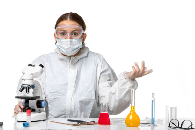 病毒前视图女医生穿着防护服 戴着口罩 用显微镜观察浅白色背景的医学病毒-健康大流行病毒套装实验室外套大流行
