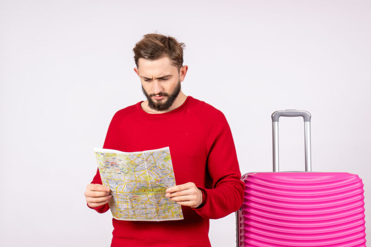 风景正面图：年轻男性 带着粉色的包 拿着白色墙上的地图旅行彩色度假飞行旅行夏季游客成人谷类食品年轻男性
