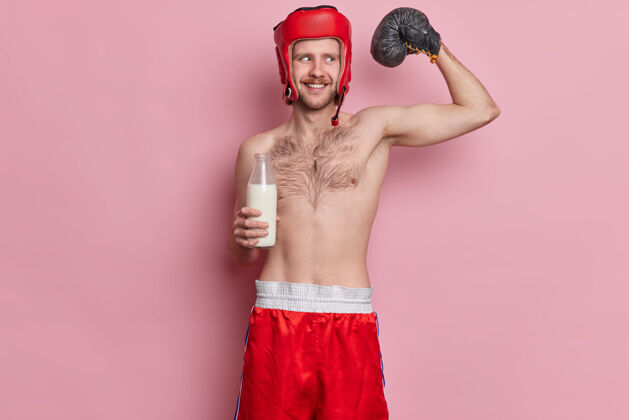 躯干有趣的男性瘦身拳击手举起手臂 展示肌肉想要达到伟大的运动效果的姿势与裸体喝牛奶运动短裤站立