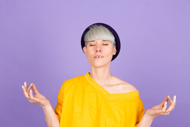位置紫色墙上的时髦欧洲女人放松 微笑着用手指做冥想姿势冷静手势瑜伽
