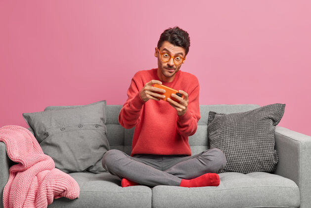 粉色上瘾的男人在智能手机上玩网络游戏 盘腿坐在舒适的沙发上地板坐着公寓