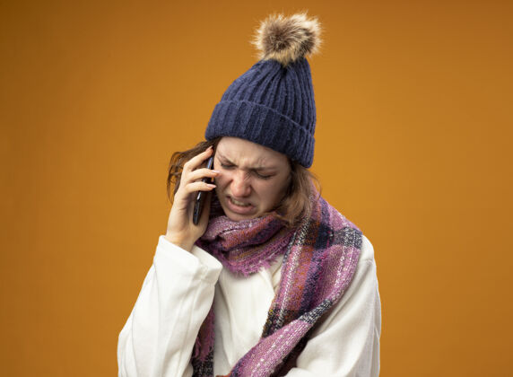 围巾穿着白色长袍 戴着带围巾的冬帽 在橘色墙上孤独地讲着电话女孩电话说话