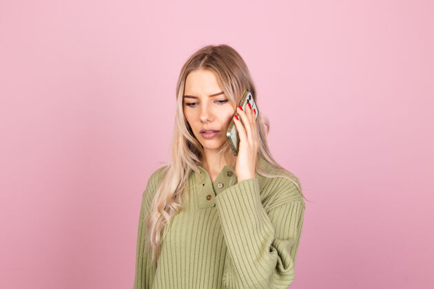 脸漂亮的欧洲女人在粉红色的墙上穿着休闲针织毛衣年轻压力手机