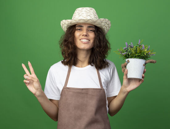 穿身着制服的年轻女园丁微笑着 戴着园艺帽 在花盆里捧着花 在绿色的草地上表现出与世隔绝的和平姿态和平女性园艺