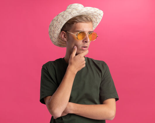 年轻想着看着身边穿着绿衬衫戴着眼镜戴着帽子的年轻帅哥把下巴孤立在粉红色的墙上思考下巴壁板