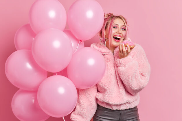 满意积极向上的年轻女孩带着亮粉色的妆容咬着美味的甜甜圈外套女孩姿势