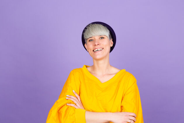 年轻紫色墙上的时髦的欧洲女人幸福的脸微笑着交叉双臂看着相机自信时尚头发