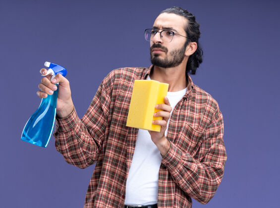 清洁想着年轻帅气的清洁工穿着t恤拿着喷雾瓶用海绵隔离在蓝色的墙上家伙年轻穿