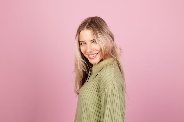 年轻漂亮的欧洲女人在粉红色的墙上穿着休闲针织毛衣时尚运动调情