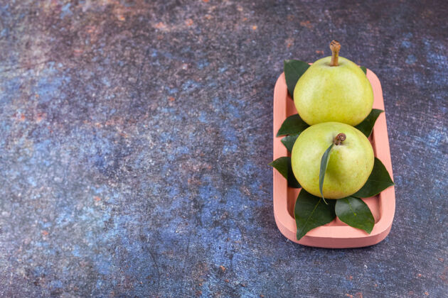 自然两个成熟的绿梨 叶子放在粉红色的木板上水果素食者食物