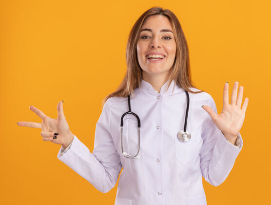 女性微笑的年轻女医生穿着医用长袍 听诊器显示不同的数字隔离在黄色的墙上长袍微笑穿
