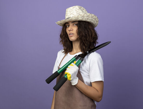 年轻自信的年轻女园丁穿着制服 戴着园艺帽和手套 肩上拿着剪刀帽子戴花园