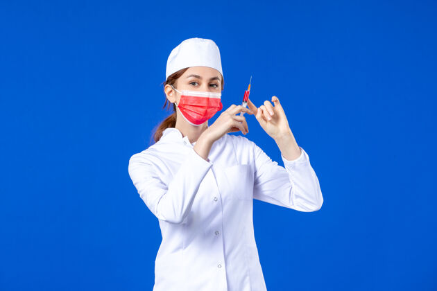 男人正面图：身穿白色医疗服的女护士 戴着红色面罩 手上拿着蓝色针剂注射医疗面罩