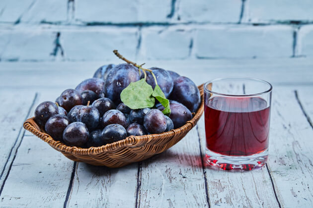 水果花园李子在一个蓝背景上的篮子与一杯果汁高品质的照片浆果石头餐桌