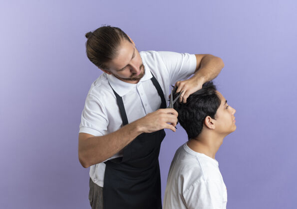 客户年轻帅气的理发师穿着制服为年轻的客户做理发隔离在紫色的背景与复制空间理发帅哥年轻