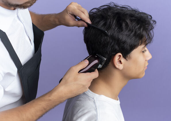 理发年轻帅气的理发师穿着制服在紫色背景上为年轻客户理发理发师年轻制服
