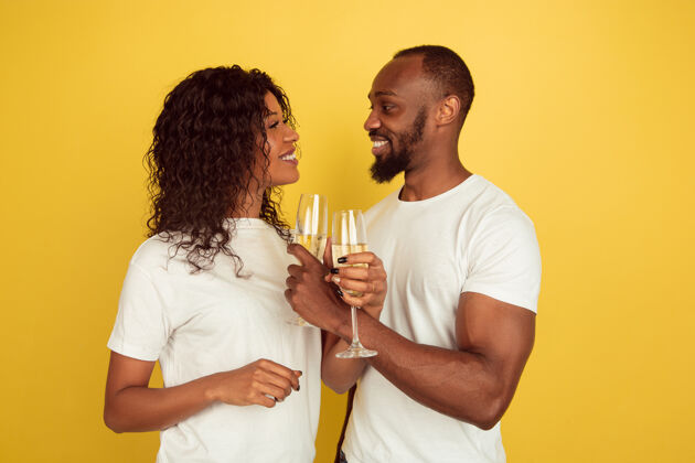情人节喝香槟情人节庆祝 快乐的非洲裔美国夫妇隔离在黄色工作室背景下人类情感的概念 面部表情 爱情 关系 浪漫的节日举行面部亲吻