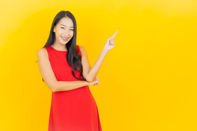 时尚肖像美丽的亚洲年轻女子穿着红色连衣裙微笑着行动在黄色的墙上黑发成人年轻