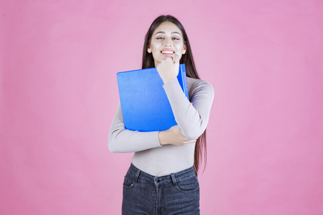 积极女孩拿着一个蓝色的项目文件夹 看起来很成功和快乐休闲成人姿势