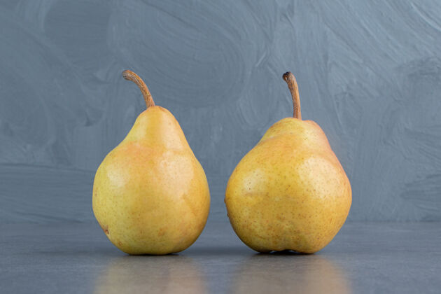 饱满两个成熟的红黄色的梨果实被隔离在一个灰色的表面上食物生的美味