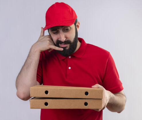 盒子年轻英俊的白人送货员身穿红色制服 戴着帽子 看着披萨盒 在白色背景上做着孤立的呼叫手势制服手势电话