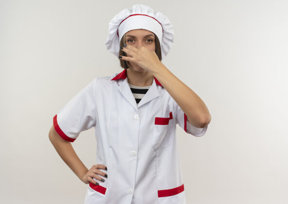 手穿着厨师制服的年轻女厨师手放在腰上举着鼻子看着隔离在白色背景上的相机 还有复印空间年轻腰女