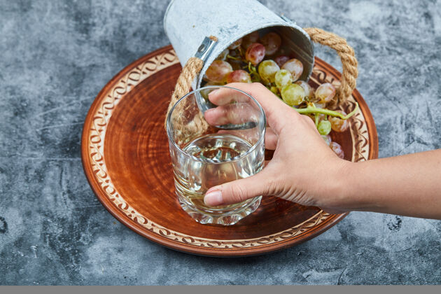 酒精手拿一杯白葡萄酒和一小桶葡萄放在大理石背景上高质量的照片手新鲜液体