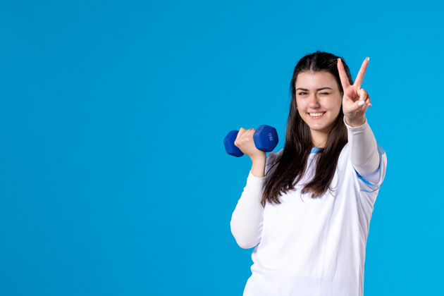 哑铃正面图快乐的年轻女性在蓝色的舞台上用蓝色的哑铃锻炼锻炼青少年身体